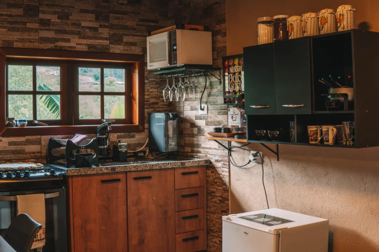 Detalhe da cozinha do chalé, com parede de pedra, fogão, micro-ondas e janela