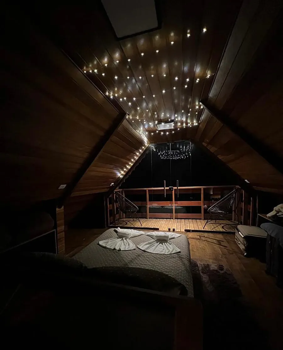 Quarto e mezanino do chalé à noite, com iluminação decorativa